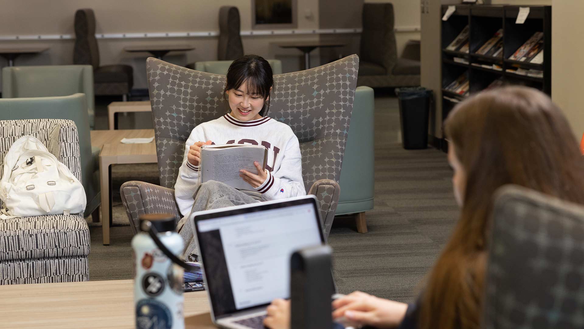 Two students studying in Meyer Library. One student is using a laptop, the other student is writing in a notebook.