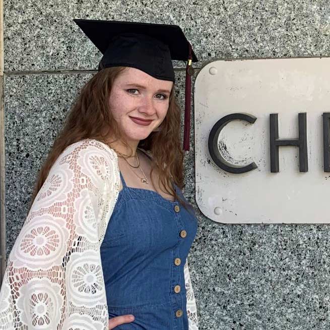 Sabrina Klement wearing her graduation mortarboard outside of Cheek Hall on campus