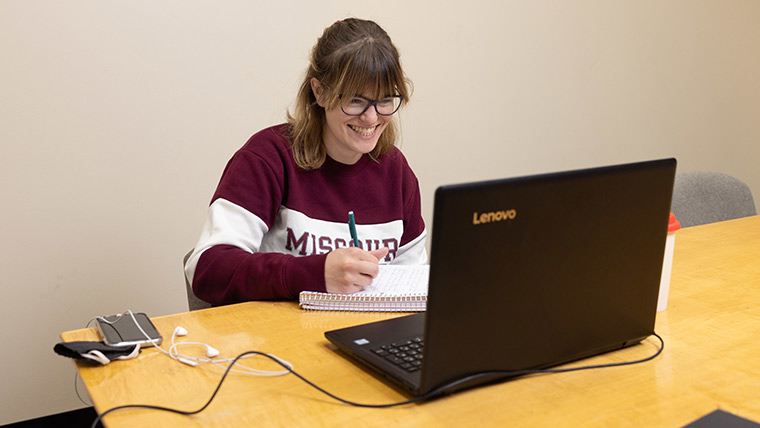 A smiling student doing homework inside Meyer Library.
